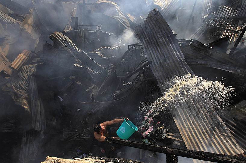 Манила, Филиппины. Мужчина помогает пожарным тушить огонь, вспыхнувший в трущобах