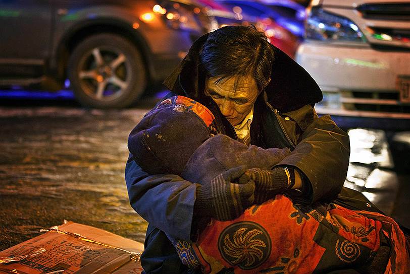 Шэньян, провинция Ляонин, Китай. Мужчина, обнимающий свою мертвую жену на улице в центре города. Он просидел с телом жены, скончавшейся от сердечного приступа, более двух часов, пока не пришел их сын и не уговорил перенести тело домой