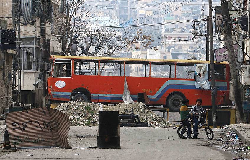 Алеппо, Сирия. Дети играют возле автобуса, с помощью которого повстанцы перегородили одну из улиц района  Бустан аль-Каср 