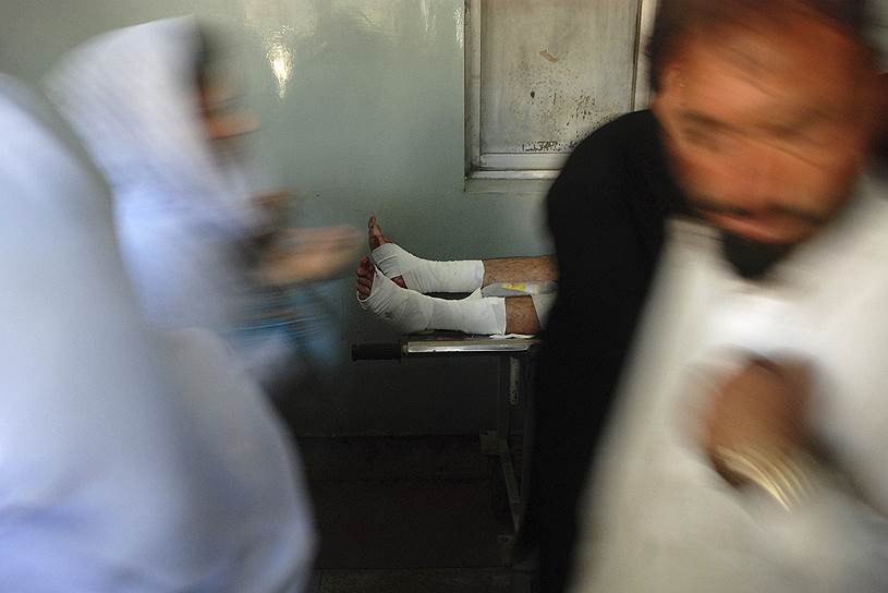 Пешавар, Пакистан. Люди проходят мимо лежащего на носилках человека, который был ранен в результате взрыва в шиитской мечети