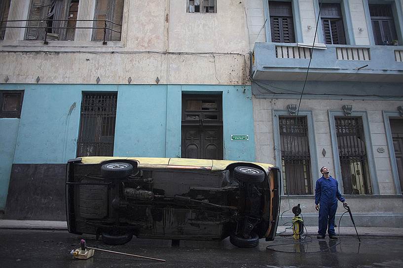 Гавана, Куба. Мужчина моет днище своего автомобиля «Москвич»