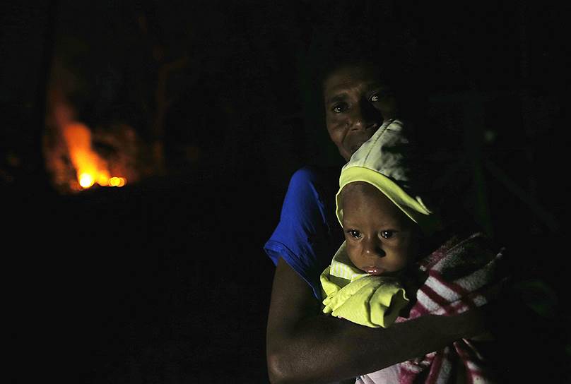 Порт-Вила, Вануату. Женщина держит на руках своего трехлетнего ребенка на фоне разрушенного дома и пожара после мощного циклона Пэм