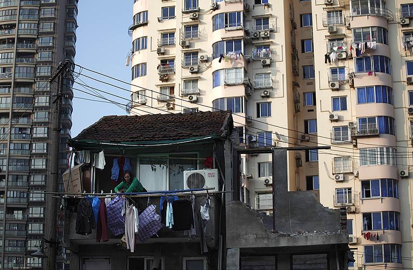 Женщина стоит на балконе своего дома в Шанхае, который должен быть снесен. На освободившейся территории построят современный жилой косплекс 
