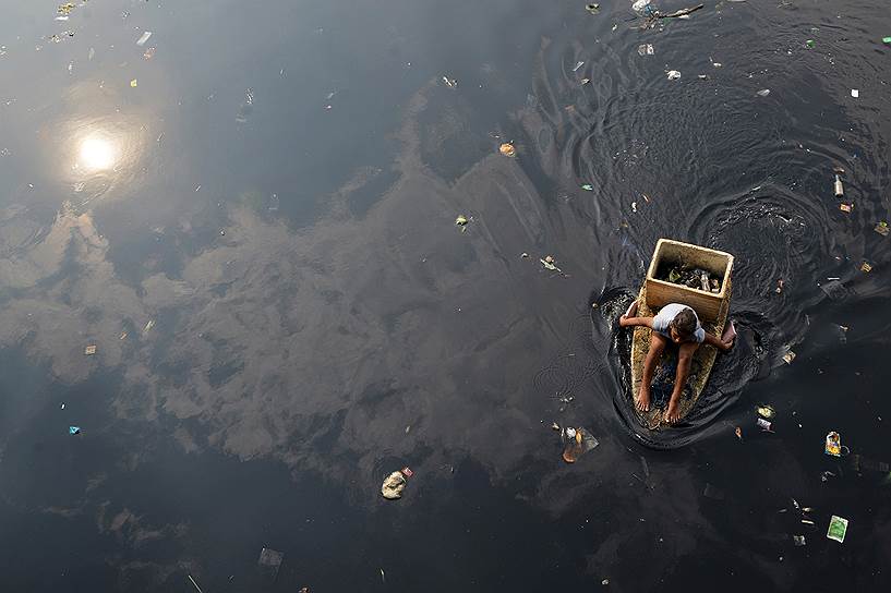 Манила, Филиппины. Женщина в самодельной лодке во время сбора мусора, годного для переработки, из загрязненной реки