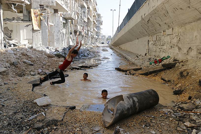 Автор: Катан Осам. Бассейн на улице: дети играют в воронке от бомбовых ударов авиации режима Башар аль-Асада (Сирия) 