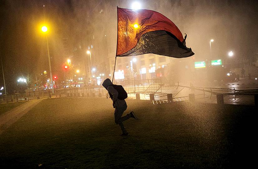 Сантьяго, Чили. Демонстрант бежит от струй водяных пушек, применяемых полицией для разгона студенческой акции протеста