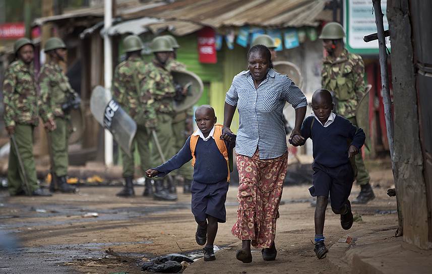 Женщина ведет детей в школу после того, как полиция распылила слезоточивый газ на улицах Найроби (Кения) во время массовых протестов