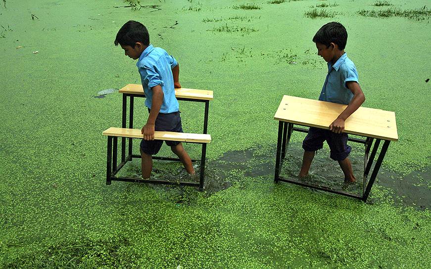 Ученики школы в индийской деревне Басы Калан несут свои парты после того, как на деревню обрушилось наводнение, а школа была затоплена 