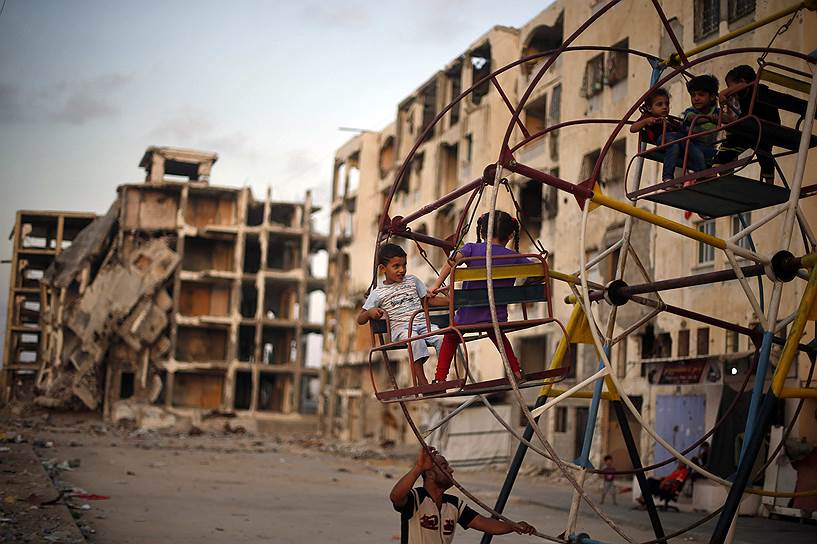 Сектор Газа, Палестина. Палестинские дети катаются на маленьком колесе обозрения возле руинов жилых домов, которые, по словам свидетелей, были разрушены израильскими обстрелами летом прошлого года