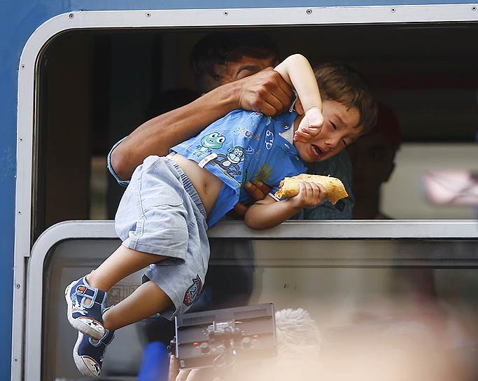 Мужчина затаскивает ребенка в окно поезда, отправляющегося с вокзала Келети в Будапеште