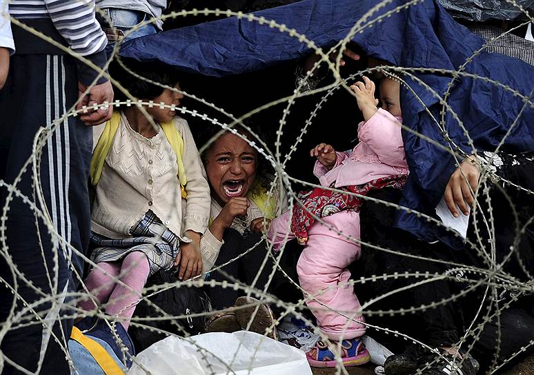 Маленькая девочка плачет, пытаясь укрыться от дождя на границе Греции и Македонии