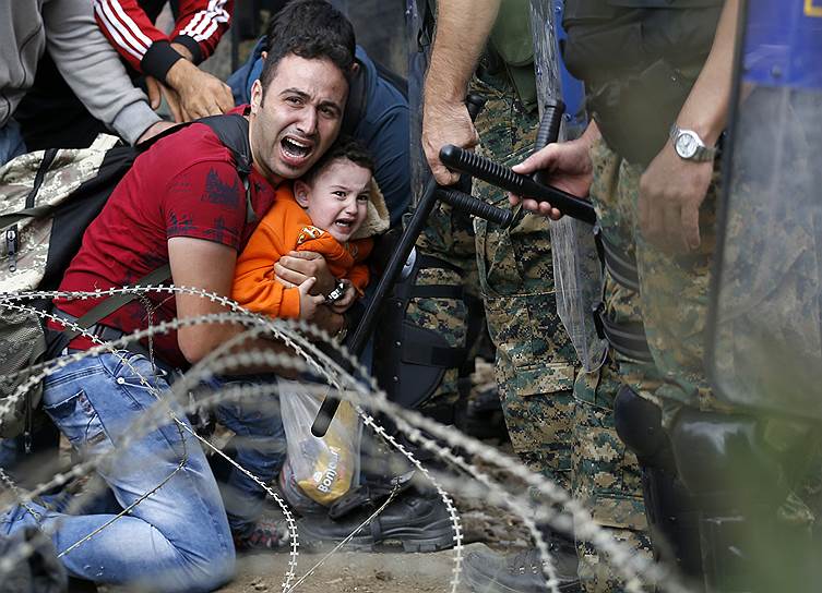 Мужчина с ребенком во время столкновений между полицией Македонии и мигрантами, которые ждут разрешения пересечь границу возле железнодорожного вокзала в Идомени (Греция) 