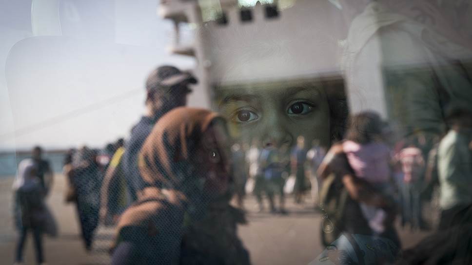 Девочка смотрит из окна автобуса на беженцев, прибывших в порт Пирея