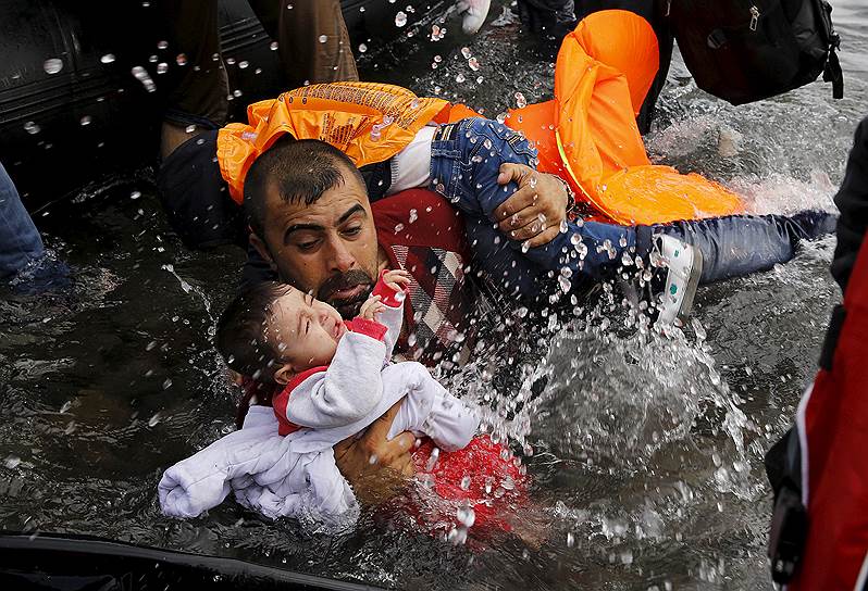 Лесбос, Греция. Сирийский мигрант с ребенком, пытающийся выбраться из резиновой лодки у берега