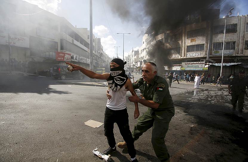Хеврон, Палестина. Сотрудник службы безопасности Палестины останавливает мальчика от броска камня по израильским солдатам во время столкновений