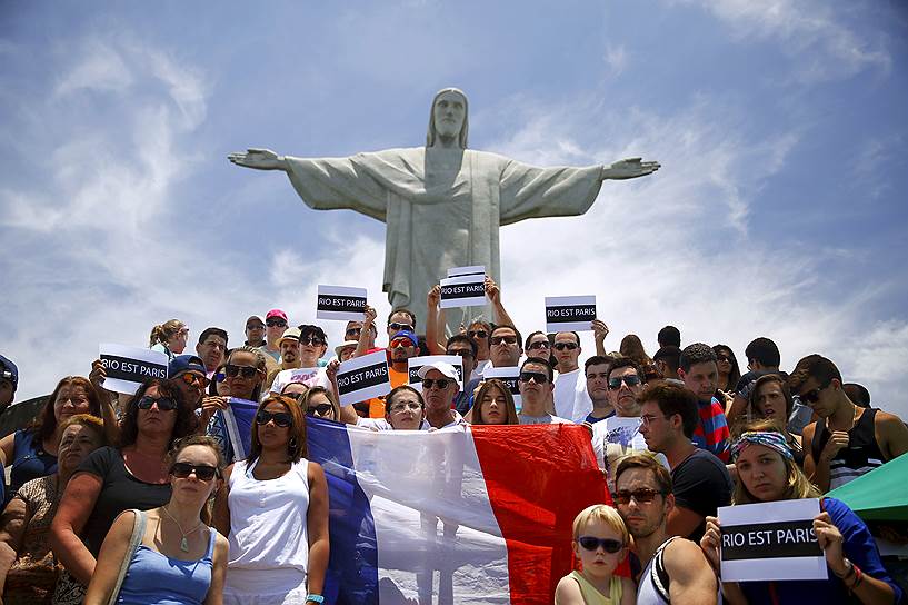 Люди держат плакаты «Рио — это Париж» и французский флаг у статуи Христа в Рио-де-Жанейро