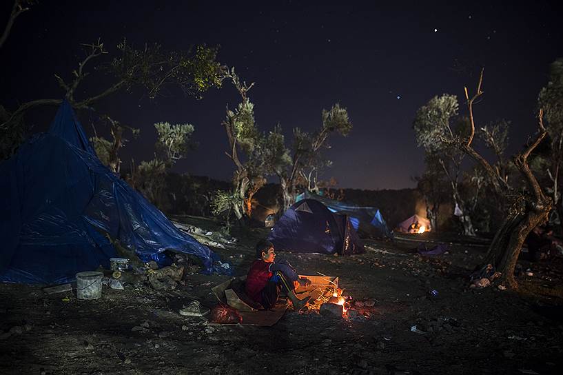 Лесбос, Греция. Беженец из Афганистана греется возле костра во временном лагере мигрантов, прибывших на остров из Турции