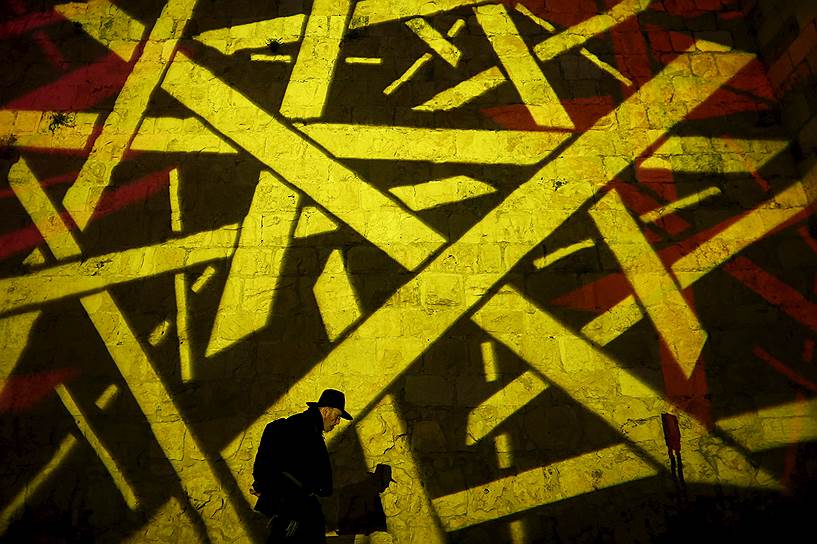 Иерусалим, Израиль. Мужчина идет мимо стены, на которую спроецирован абстрактный рисунок во время праздника Ханука