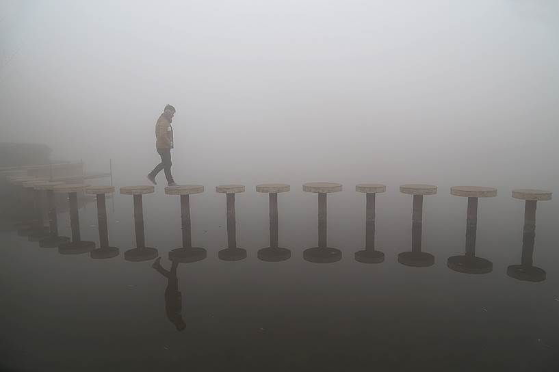 Парк Цзыся, уезд Вэньсянь, Китай. Человек, идущий по мосту во время сильного смога