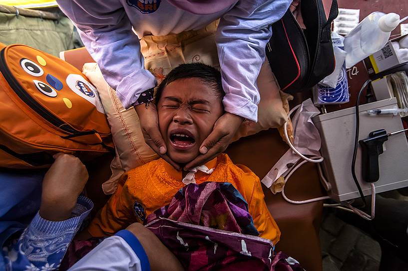 Суматра, Индонезия. Мальчик кричит во время обрезания на бесплатной массовой церемонии обрезания, организованной для беженцев от извержения вулкана Синабунг
