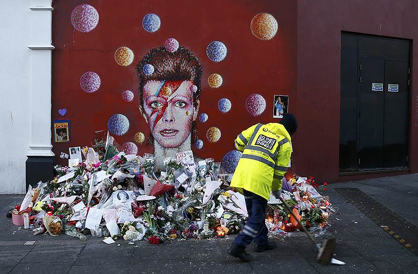 Лондон, Великобритания. Рабочий подметает тротуар в Брикстоне рядом с изображением Дэвида Боуи, куда поклонники музыканта принесли цветы, чтобы почтить его память