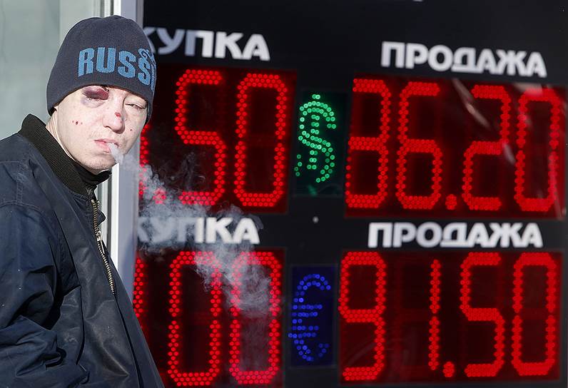  Мужчина курит возле табло обменника валюты в Москве
