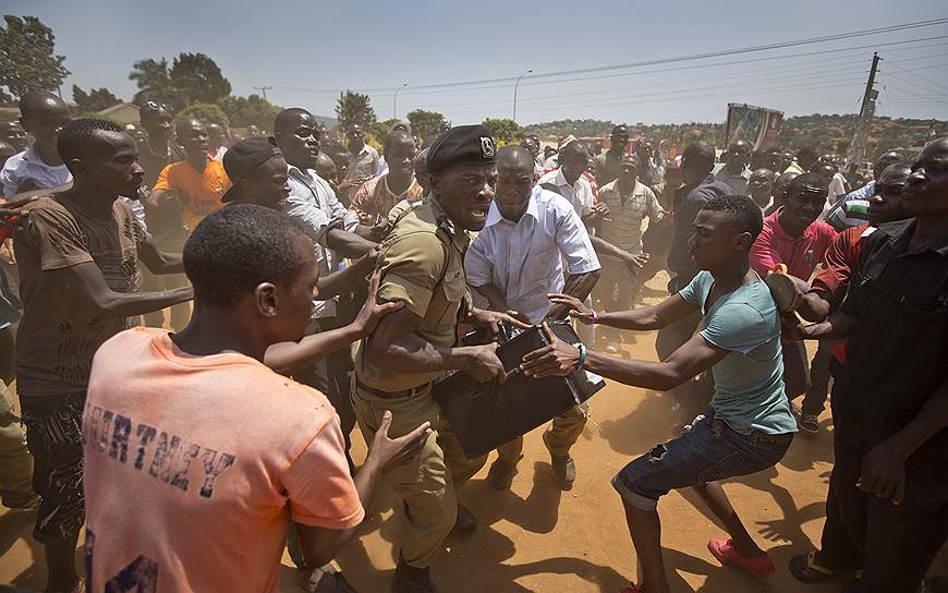Кампала, Уганда. Полицейский, несущий бюллетени, прорывается через толпу разъяренных граждан, прождавших более 7 часов у избирательного участка из-за отсутствия форм для голосования