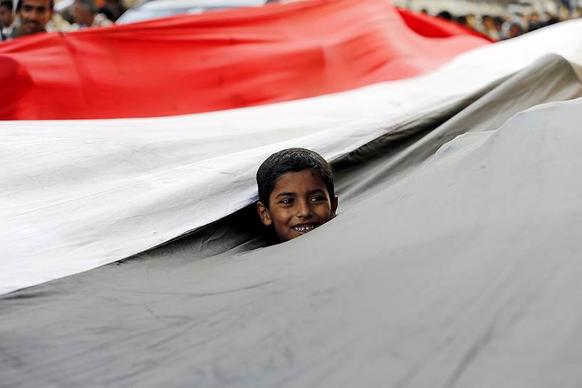 Сана, Йемен. Мальчик выглядывает из национального флага во время митинга сторонников хуситов против авиаударов саудовской коалиции