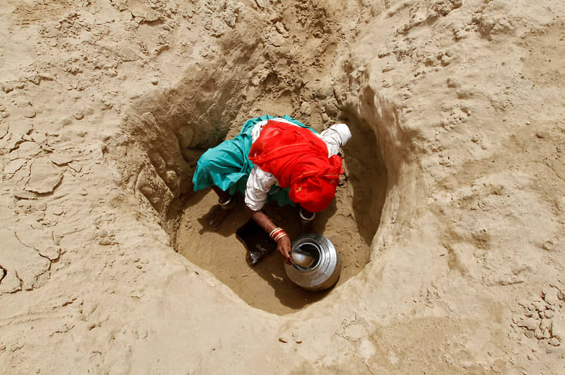 На фото: женщина наполняет кувшин питьевой водой из небольшого отверстия, сделанного вручную для сбора воды из высохшей реки Банас на западе Индии. Сельские жители ходят 2,5 км, чтобы набрать питьевой воды, для этого им требуется не менее 30-40 минут