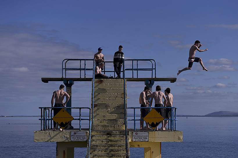 Голуэй, Ирландия. Молодые люди, ныряющие в море с вышки на пляже Солтхилл