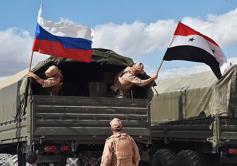 Российские военнослужащие устанавливают флаги России и Сирии на кузове грузовика перед раздачей гуманитарной помощи 
