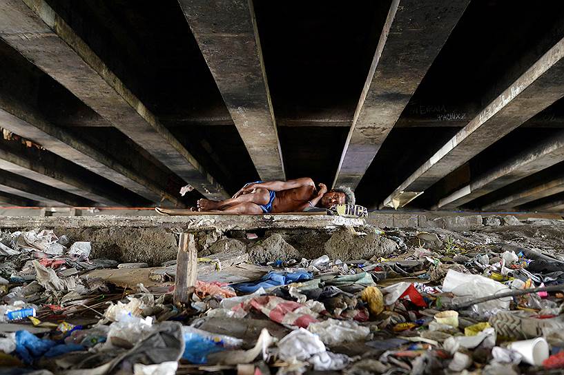 Паранак, Филиппины. Мужчина, спящий под мостом среди гор мусора