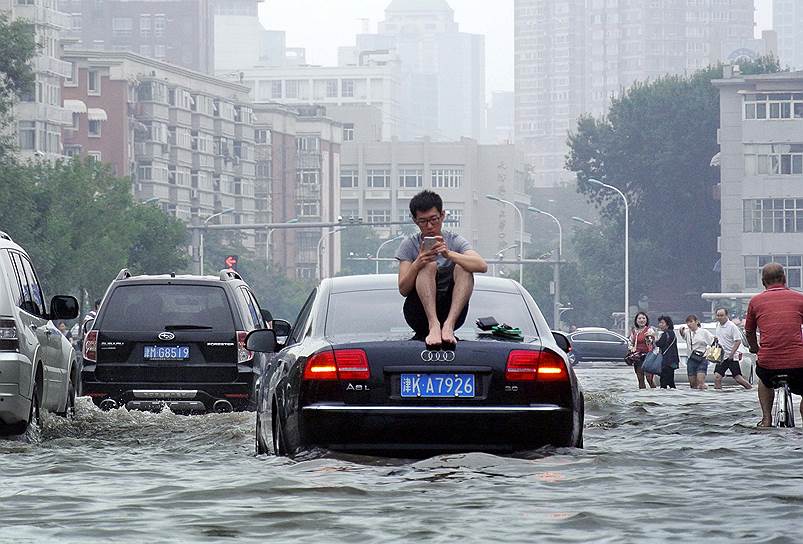 Тяньцзинь, Китай. Мужчина сидит на крыше автомобиля во время наводнения 