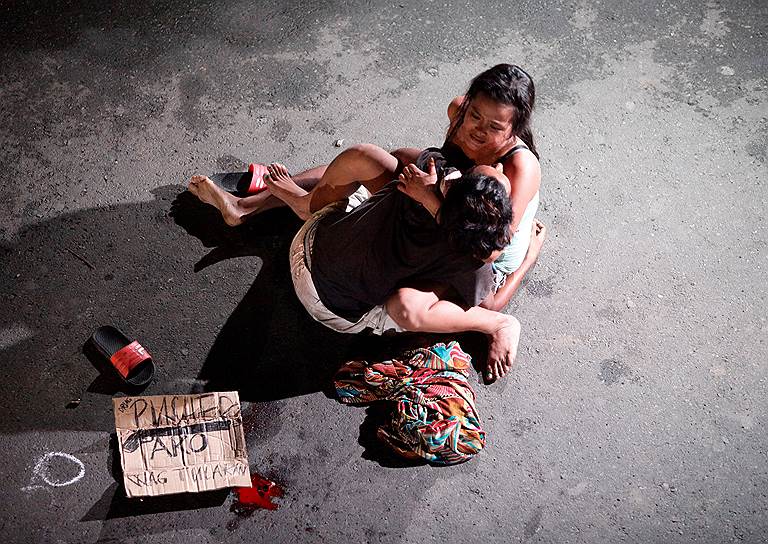 Манила, Филиппины. Женщина держит на руках тело своего мужа, которого убила на улице группа «мстителей», борющихся с наркоторговлей. Надпись на картонке: «Я торговец наркотиками»