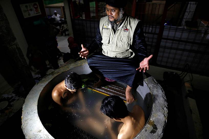 Пурбалингга, Индонезия. Руководитель центра традиционной медицины молится за выздоровление двух наркоманов, которые сидят в лекарственной ванной 