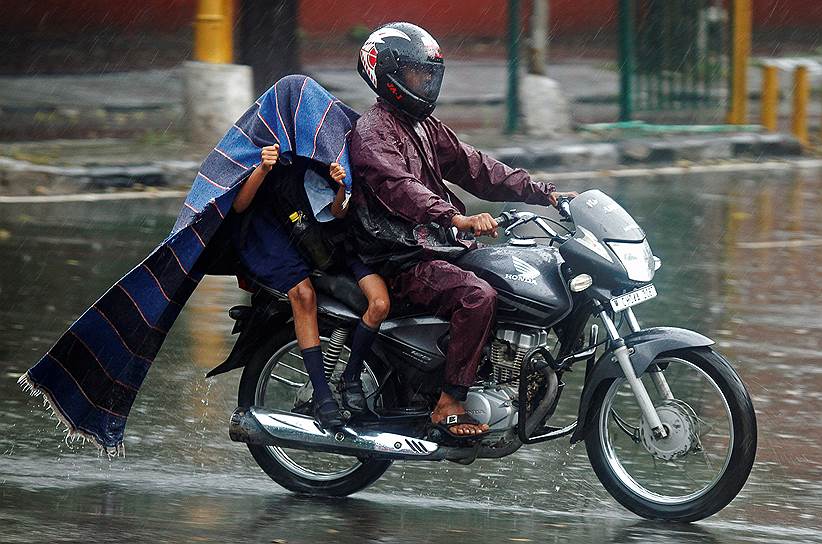 Чандигарх, Индия. Дети, прячущиеся от дождя во время поездки на мотоцикле со своим отцом во время ливня