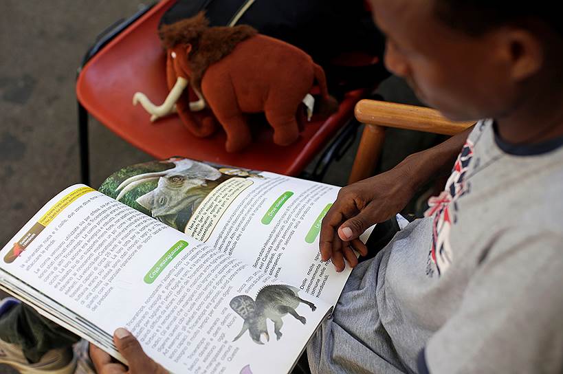 Беженец читает книгу о динозаврах в приюте «Баобаб» в Риме