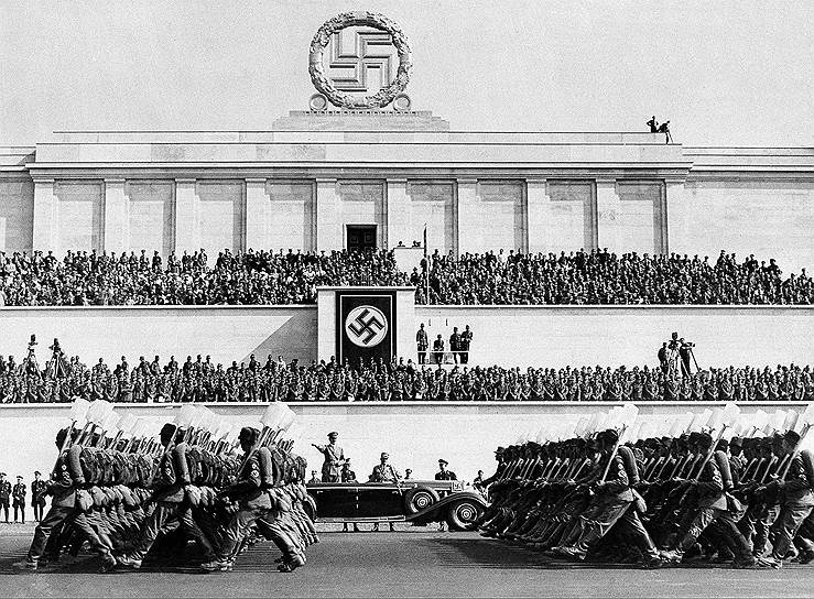 24 апреля 1945 года, на четвертый день оккупации Нюрнберга, американские войска провели у трибуны военный парад. В финале торжества была взорвана свастика, которая венчала конструкцию&lt;br>На фото: Адольф Гитлер принимает парад в 1937 году