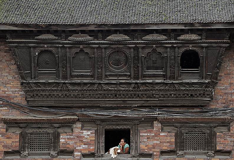 Бхактапур, Непал. Женщина с собакой сидит у окна