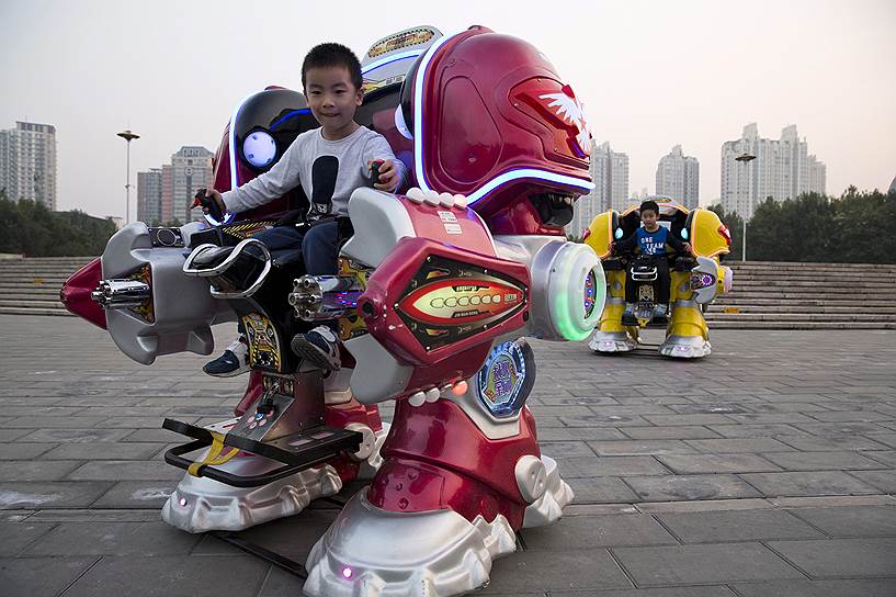 Пекин, Китай. Ребенок катается на роботе по парку 