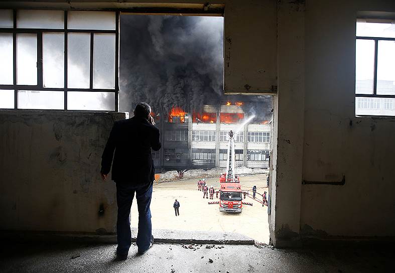 Стамбул, Турция. Мужчина смотрит, как пожарные тушат огонь на фабрике по производству пластика