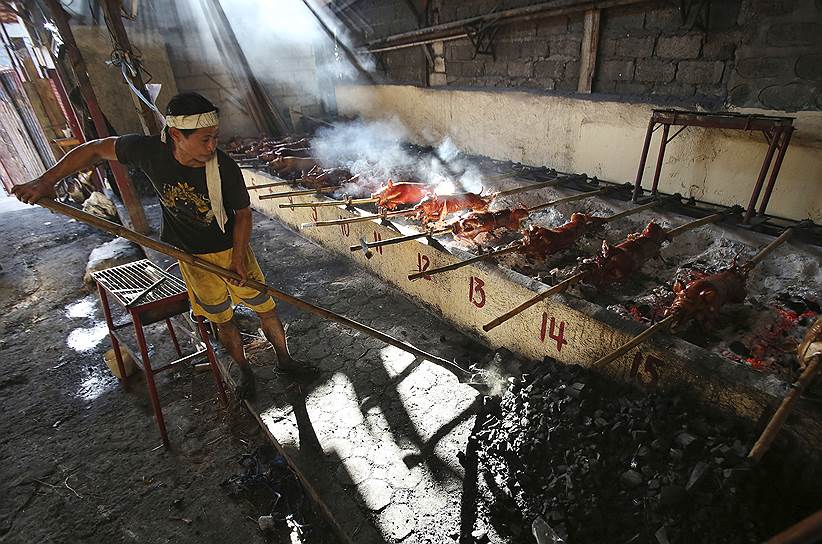 Манила, Филиппины. Повар разжигает угли для приготовления поросят