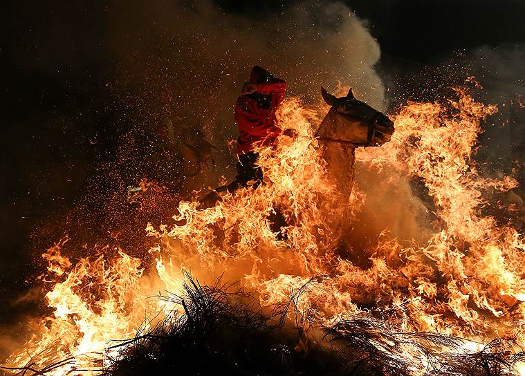 Мадрид, Испания. Участник празднования дня святого Антония прыгает на лошади через костер