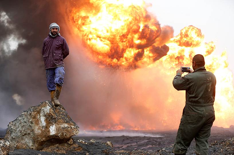 Кайяра, Ирак. Местные жители фотографируются на фоне горящего месторождения нефти, которое подожгли террористы «Исламского государства»