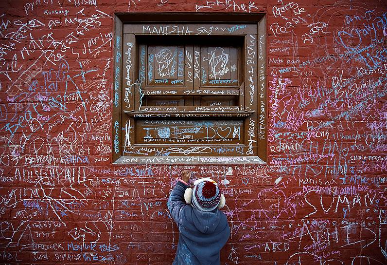 Катманду, Непал. Мальчик рисует мелом на стене храма богини Сарасвати во время религиозного праздника