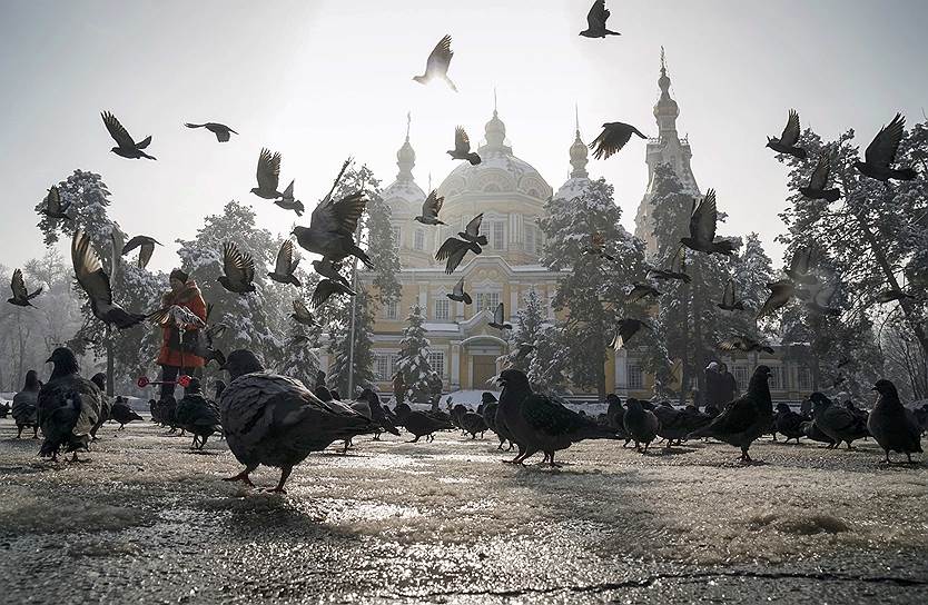 Алматы, Казахстан. Женщина кормит голубей у православного храма