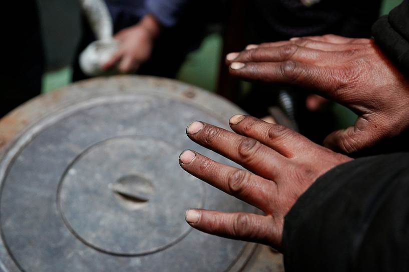 Местный житель греет руки у домашней угольной печи