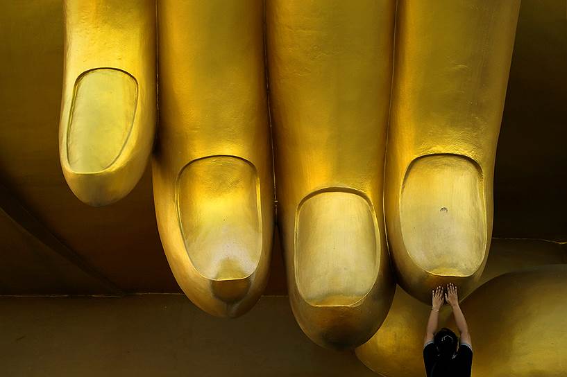 Ангтхонг, Таиланд. Женщина молится, касаясь пальца статуи Будды 