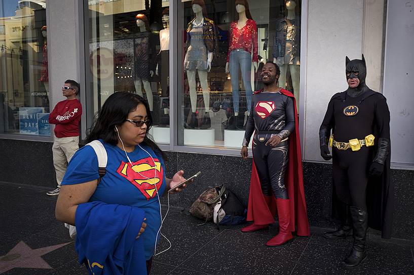 Лос-Анджелес, США. Девушка в футболке с логотипом Супермена проходит мимо уличных артистов в костюмах Супермена и Бэтмена 