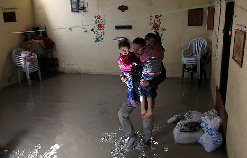 Рафах, Сектор Газа. Мужчина выносит своих детей из затопленного дождем дома